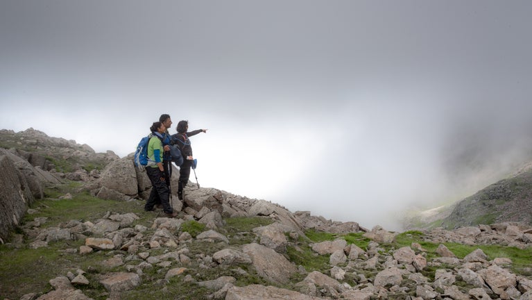 Hikers point out towards Great End from near the summit of Scafell pike on a misty summer's day